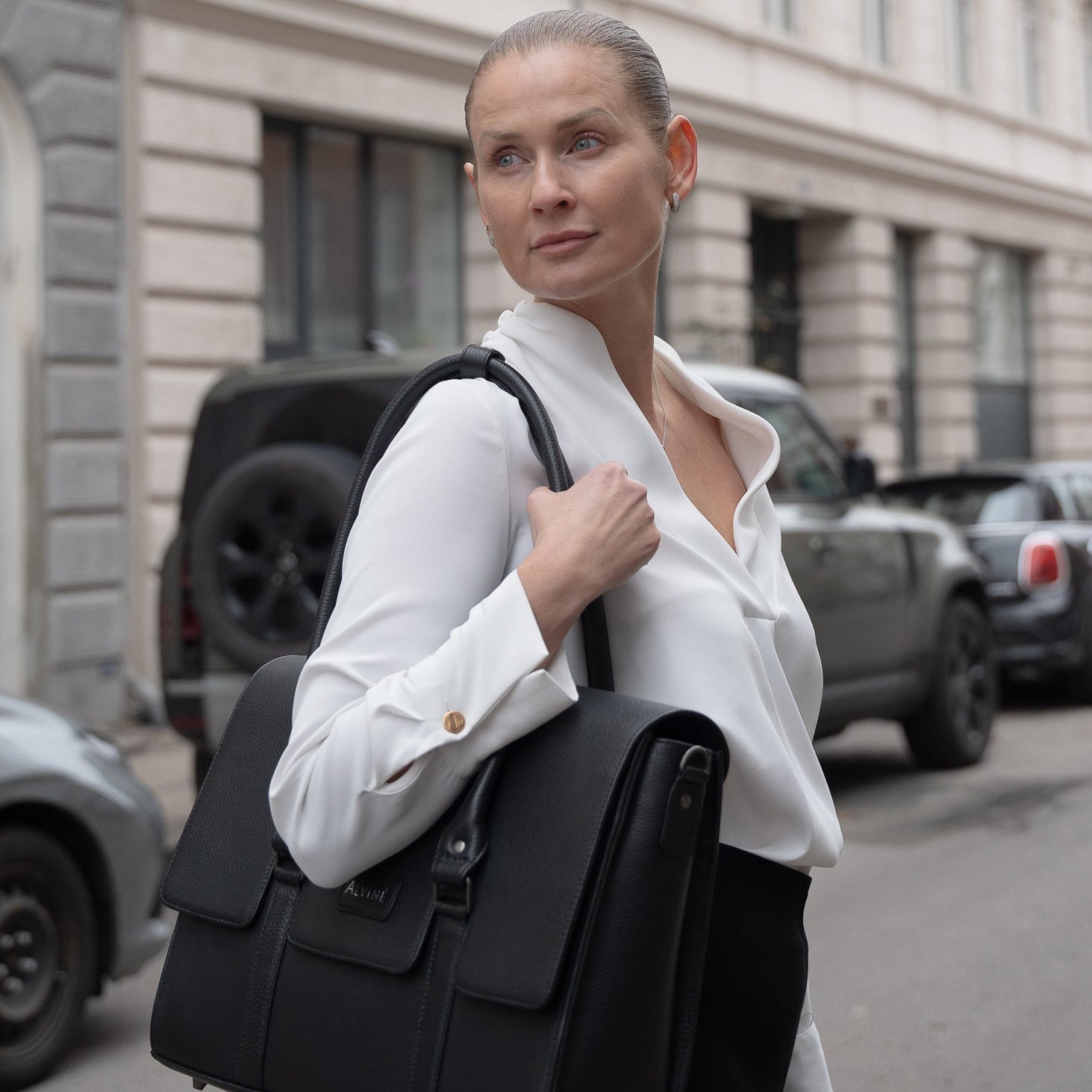 Kvinde i hvid skjorte der kigger sig over skulderen med CC Arbejdstaske i sort læder over skulderen