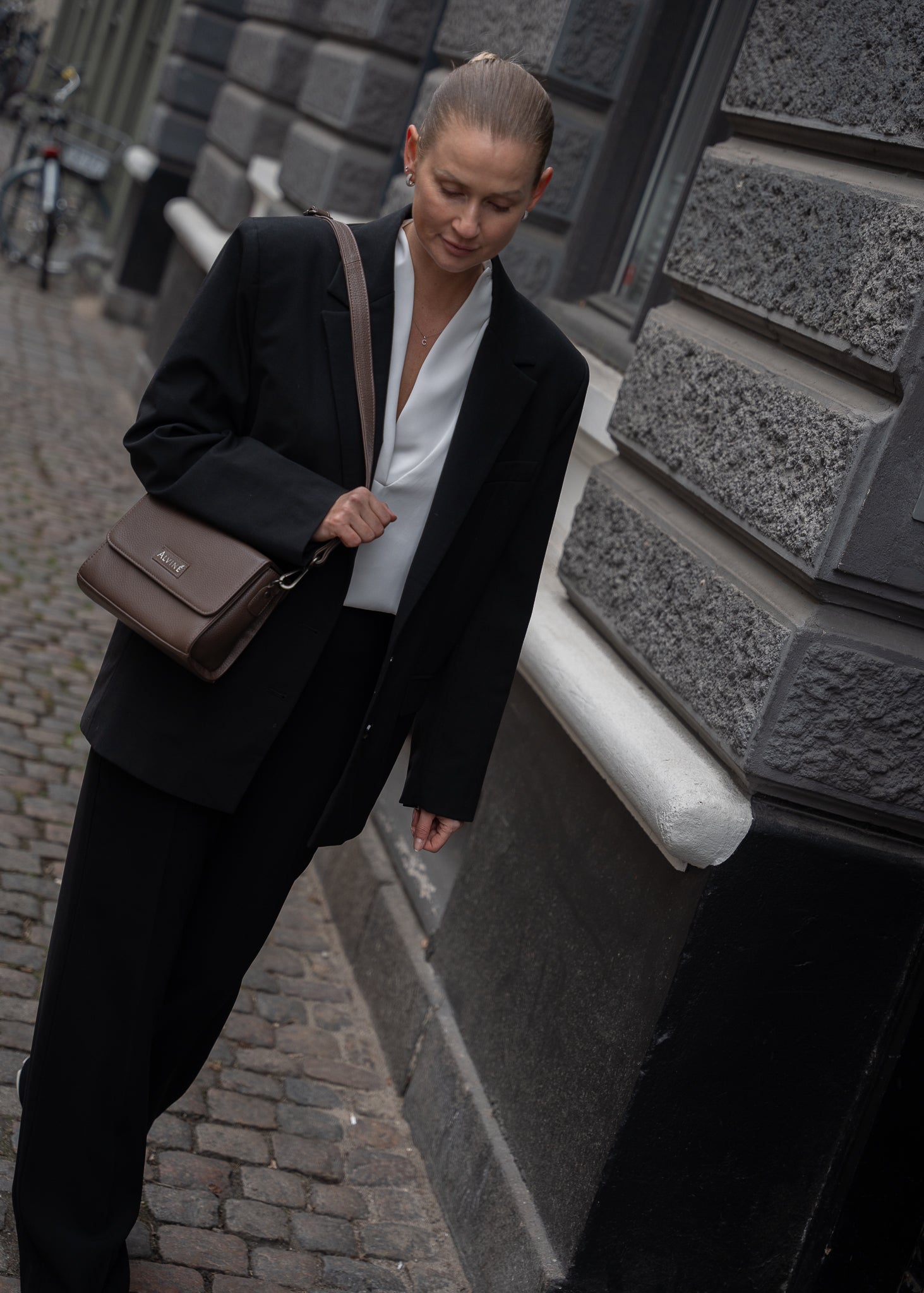 CC Pouch i Espresso læder som crossbody på kvinde i mørkt jakkesæt der går i gaden