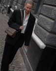 CC Pouch i Espresso læder som crossbody på kvinde i mørkt jakkesæt der går i gaden