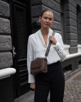 CC Pouch i Espresso læder som crossbody på kvinde i hvid skjorte der kigger ind i kameraet