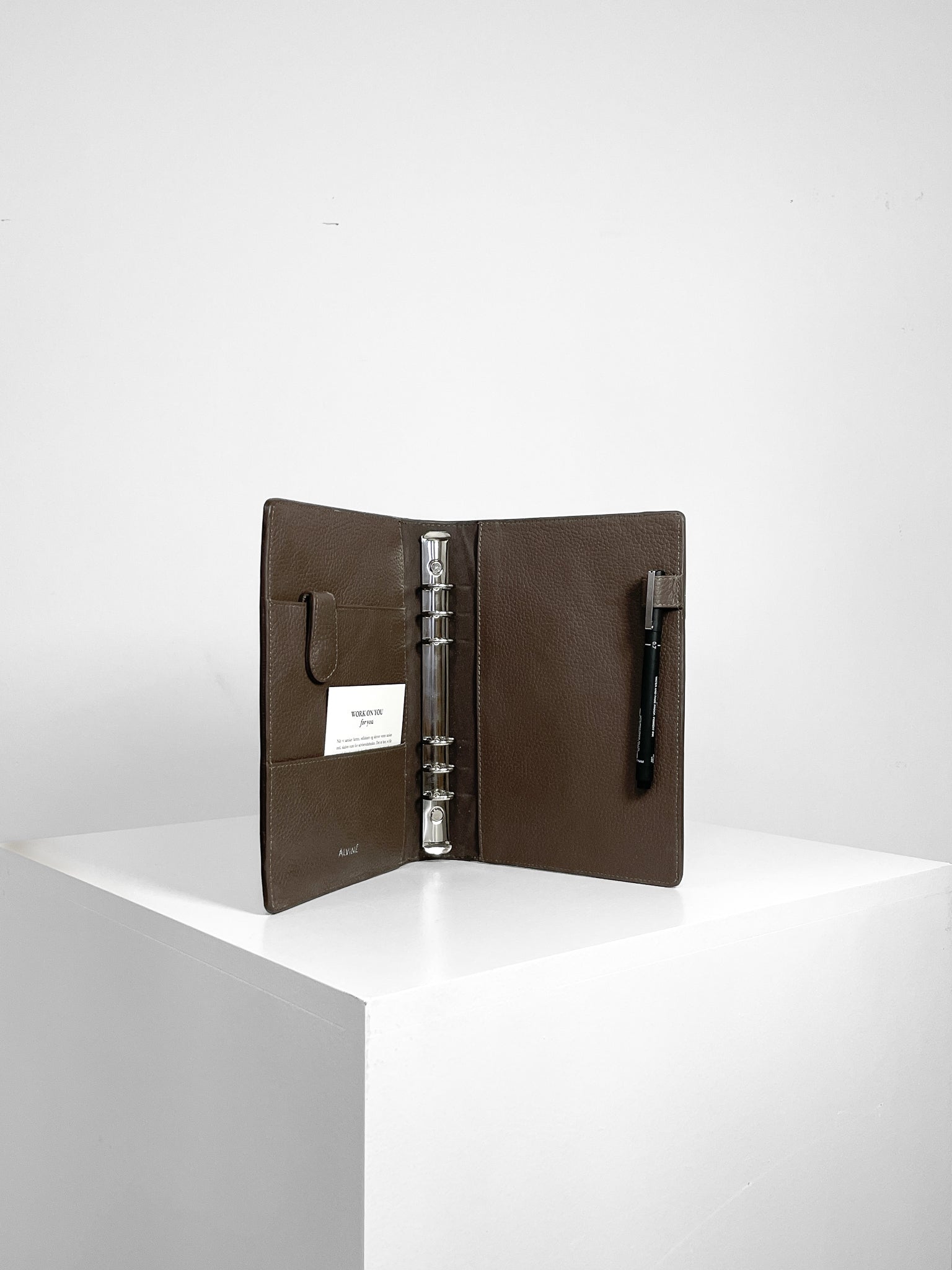 Åben Planner i Espresso læder stående uden inserts på en pedistal.