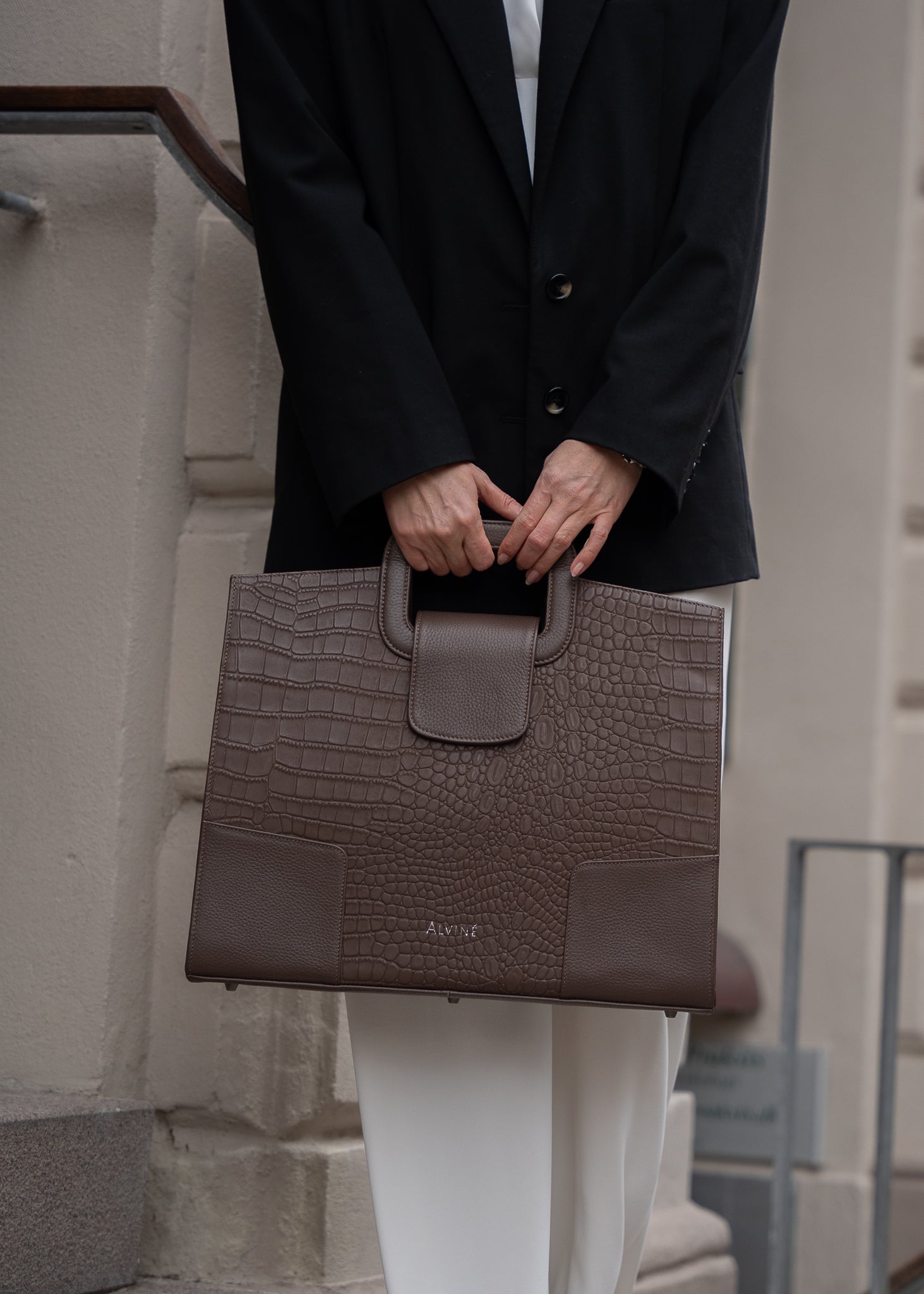 Close up af VGC Arbejdstaske i Espresso læder med krokodillestruktur i hånden på stående kvinde i en sort blazer.