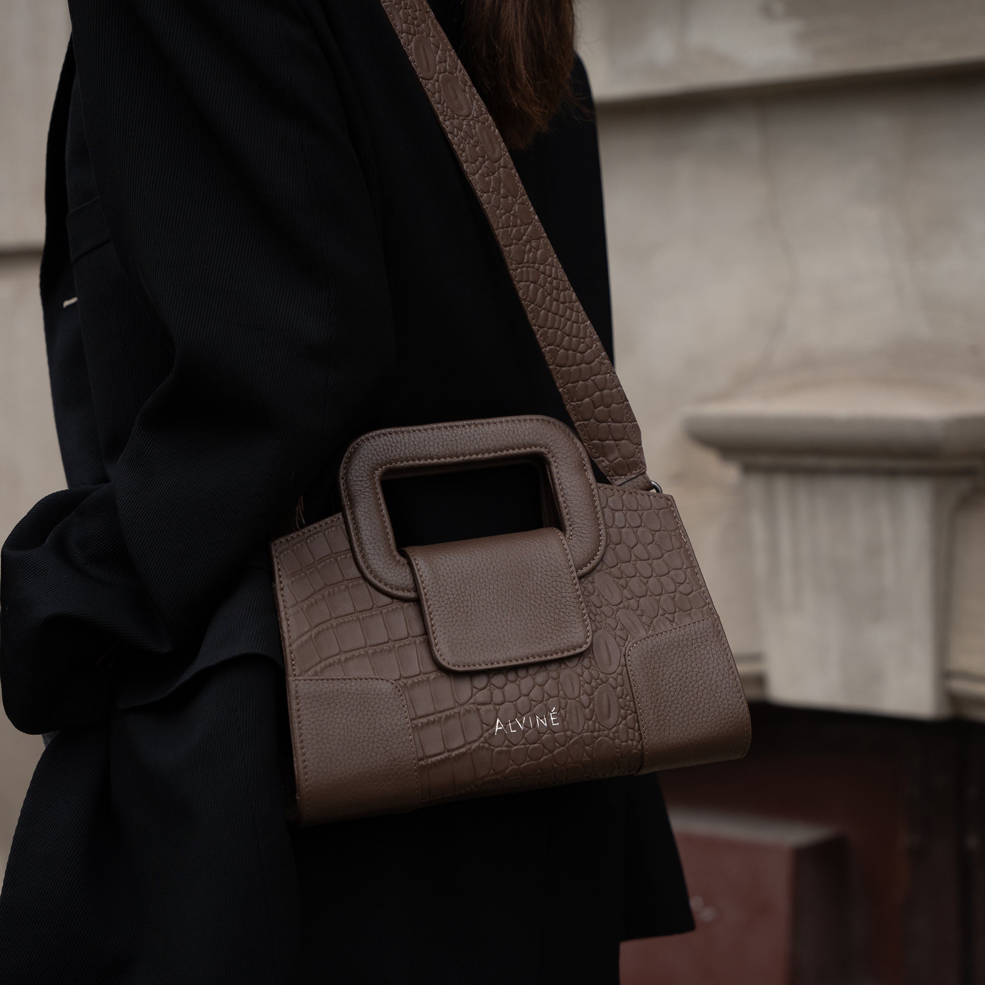 VGC Håndtasken i Espresso læder med krokodillestruktur som crossbody på kvinde i mørk jakke.