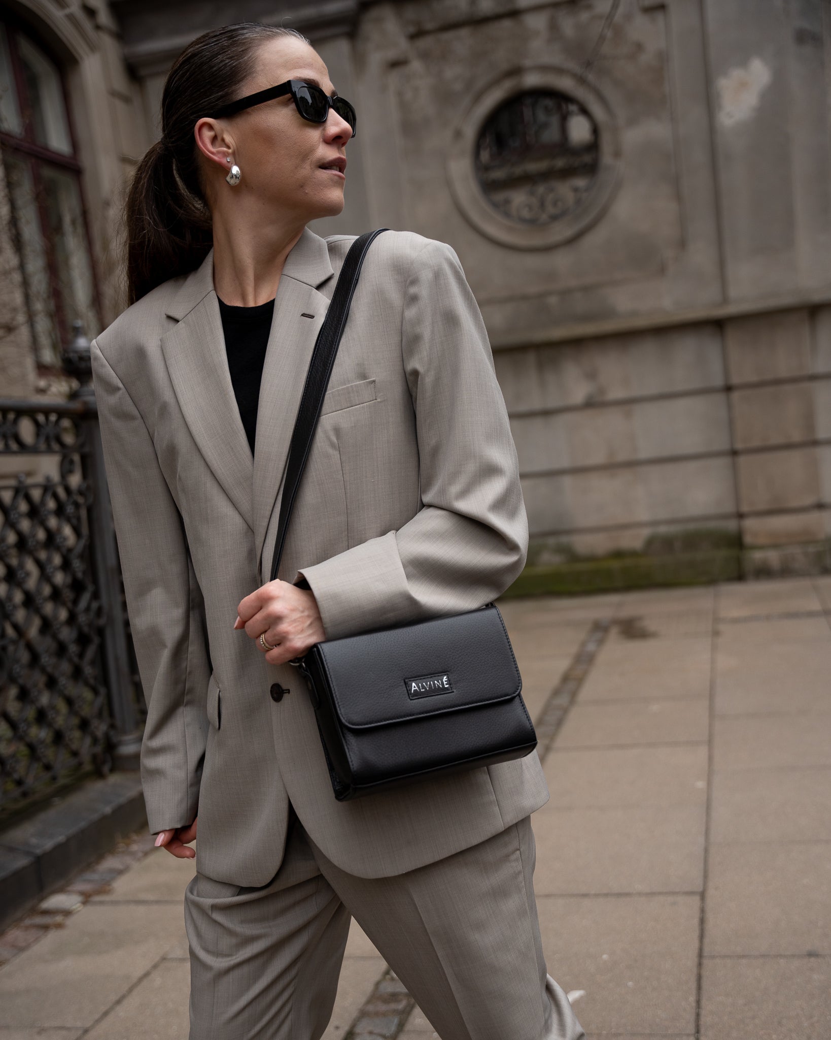 CC Clutch i sort læder som crossbody på kvinde i gråt jakkesæt