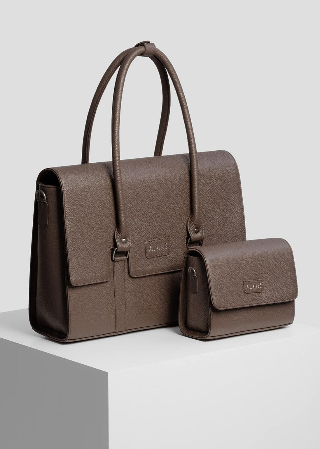 Arbejdstaske og Clutch i espresso læder fra The Classic Collection på pedestal