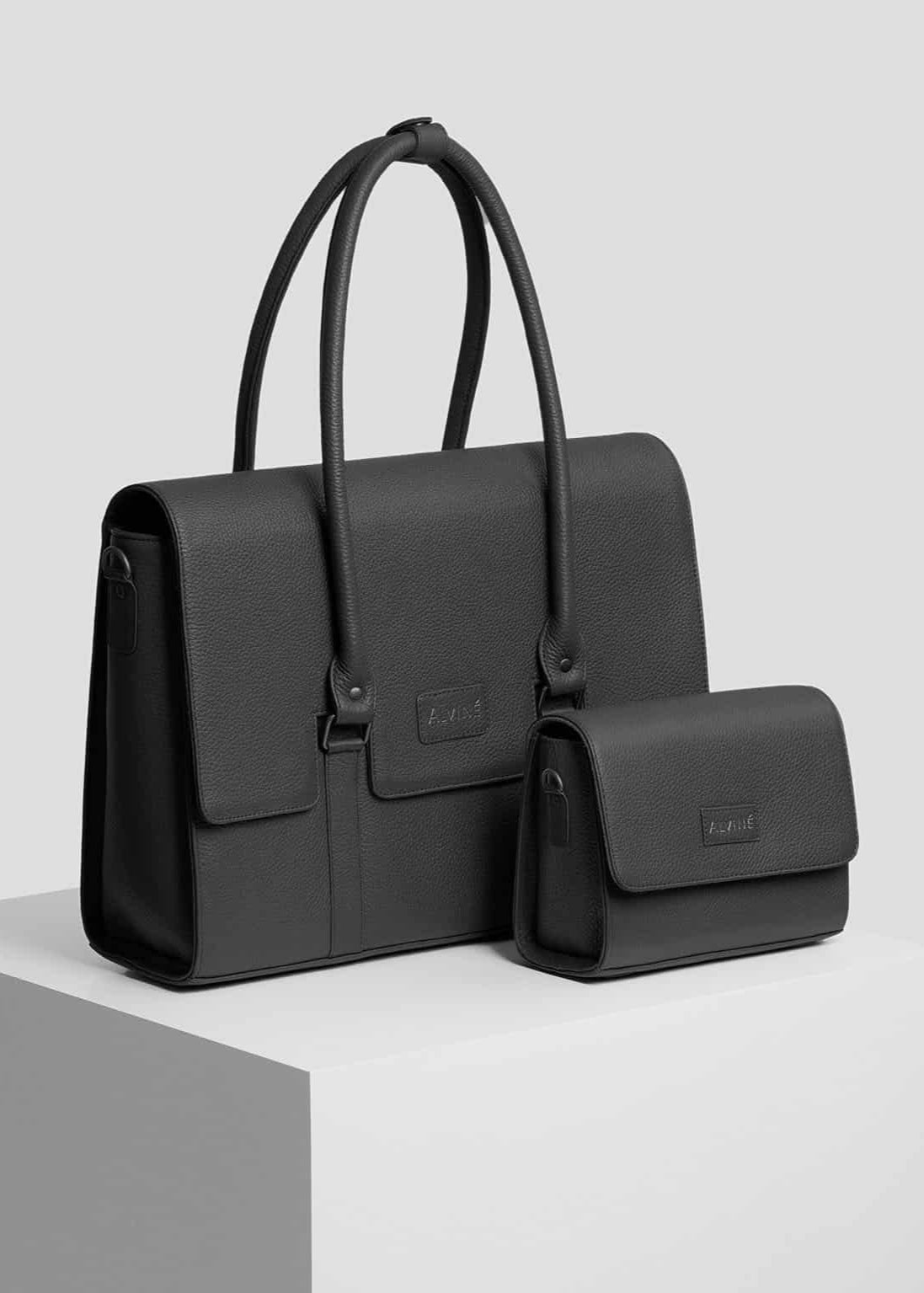 Arbejdstaske og Clutch i sort læder fra The Classic Collection på pedestal